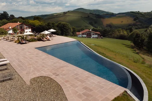 Outdoor pool with brick walkway to the left and pool chairs by a building