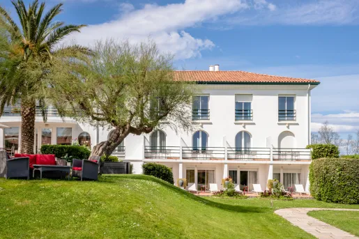 Exterior view of a white building with a grass hill in front