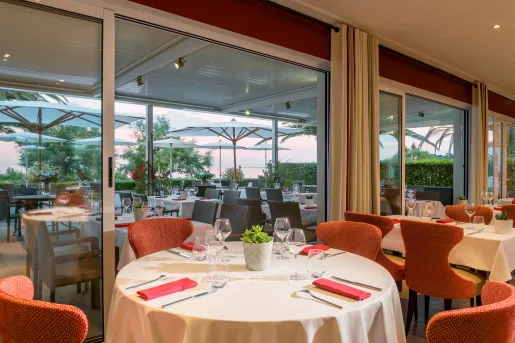 Indoor dining hall with circular tables, white cloths and red chairs