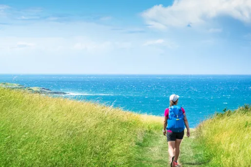 Woman hiking in a grassy field, with the ocean in the distance