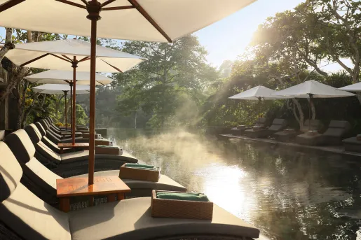 Outdoor pool surrounded by reclining chairs, white smoke on the water