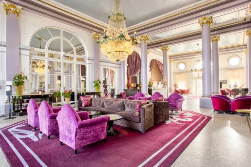 Hotel seating area with pink and gray velvet chairs and a large chandelier