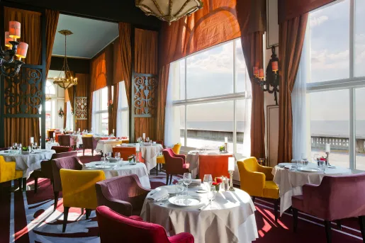 Dining hall with red and yellow cushioned chairs, and large windows with orange curtains