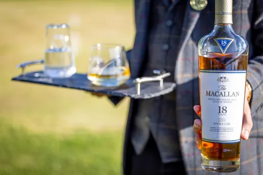 Person in a suit holding a tray of glasses and a bottle of Scotch whisky