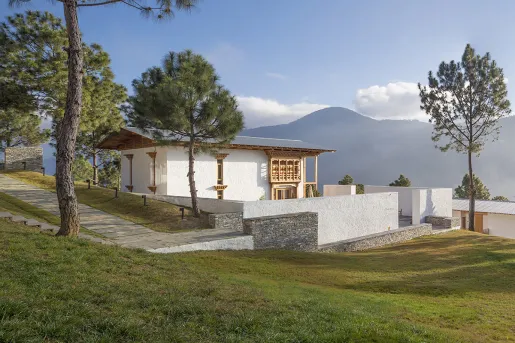 White building on a hill surrounded by trees with mountains in the distance