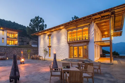 White building with a wooden balcony and outdoor patio area with tables and chairs