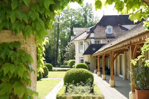 Outdoor view of white and brown building with bushes and tall trees in the background