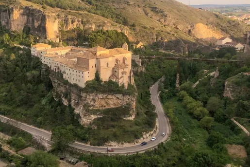 Stone, rustic building on a cliff, next to a road with a sharp curve