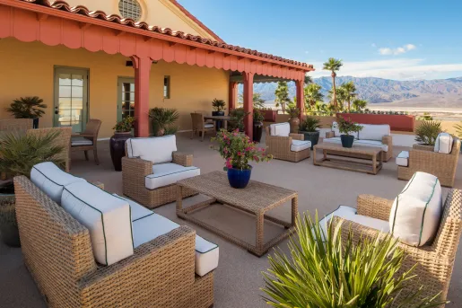 Outdoor patio with woven chairs and tables, with tall mountains in the distance