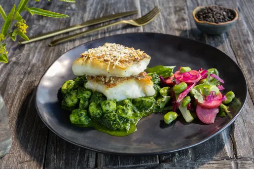 Black plate with grilled fish on top of a bed of green and pink vegetables