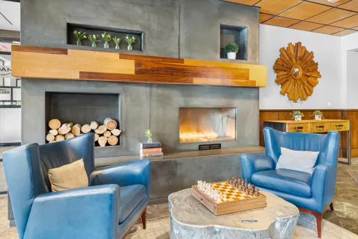 Lounge area in front of a fireplace wit blue chairs and a chess board on a table