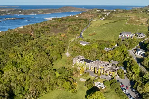 Sky view of large hotel building in the middle of a grass valley, surrounded by lush trees