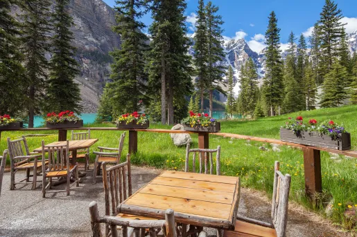 Outdoor patio with wooden chairs and tables, looking out to a lake surrounded by trees