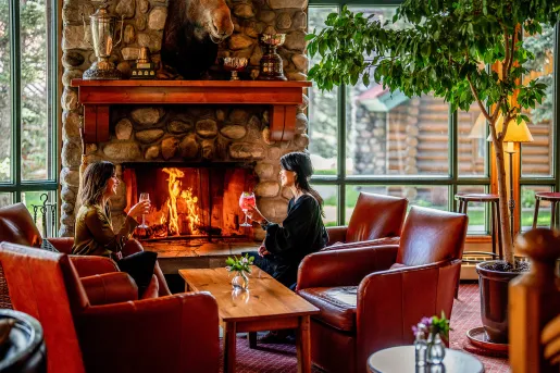 Two women holding wine glasses next to a stone fireplace