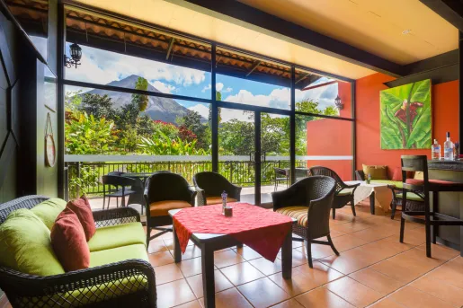 Bar and lounge with woven chairs and large glass walls and doors leading to a jungle