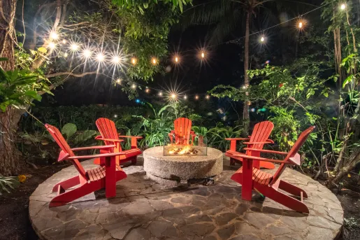 Red lawn chairs surrounding a stone fire pit outdoors on a circular rock slab