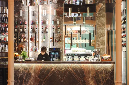Liquor bar with stone countertops and brown pillars, with a bartender behind the counter