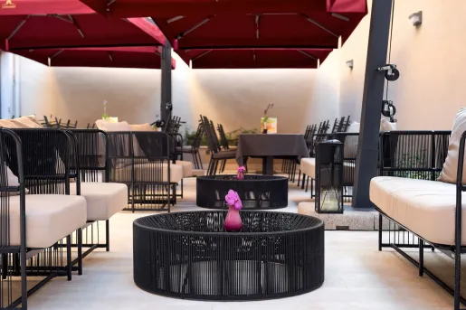 Outdoor lounge area with black, woven chairs and dining tables in the background