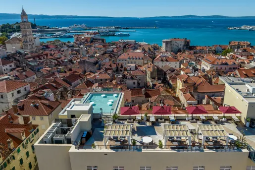Sky view of yellow buildings with orange roofs, with a building having a pool on the roof
