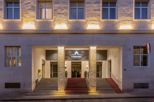 Hotel building entrance, with lights illuminating the stone wall and a red carpet on the stairs
