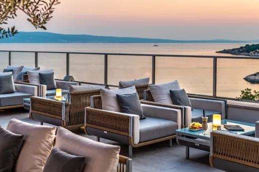 Outdoor patio with gray, cushioned chairs with a view of the ocean in the background