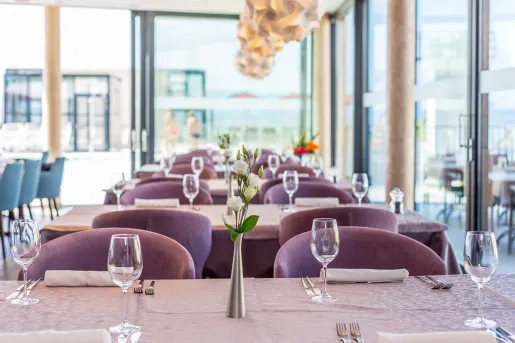 Dining hall with pueple, cushioned chairs and a vase with flowers in the center of the table