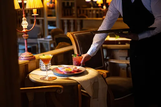 Waiter serving a red drink and a plate of food to an empty, circular table