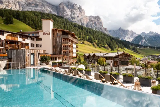 Outdoor infinity pool overlooking a hotel complex and tall, tree-covered hills