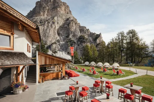 Stone and wood lodge with red chairs outside and a large mountain in the background