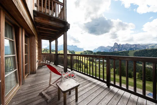 Wooden balcony with a red chair looking out towards cloud-covered mountains