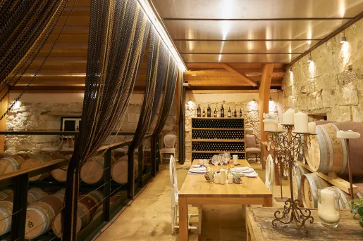 Underground cellar full of wine barrels and a table with two chairs