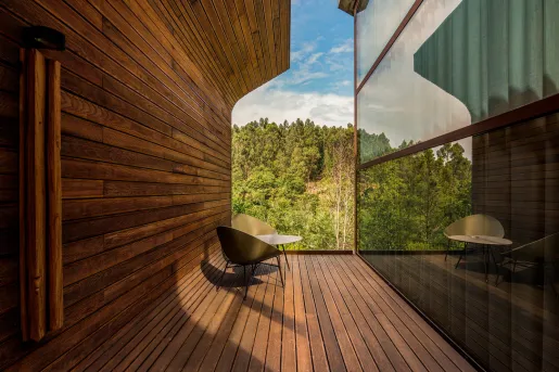 Two wooden chairs and a table in between two buildings looking out to a forest