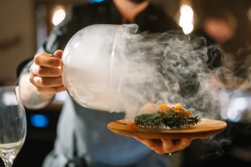 Man holding a plate of food while holding a dome of fog over the plate