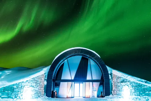 Entrance of building in the middle of a snow valley, with the Northern Lights in the sky