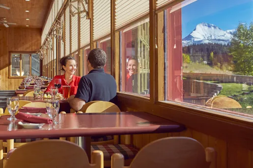 Man and woman at a dining table staring out a window towards mountains and a forest