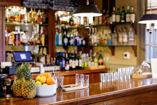 Wooden bar counter top with glasses, fruit and bottles of liquor in the background