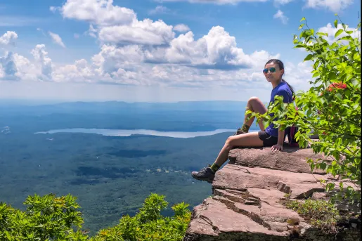 Woman sitting on a cliff with large trees on ground floor