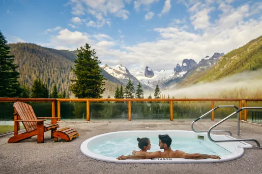 two people in a hot tub overlooking snow capped mountains