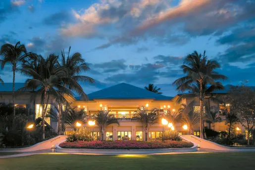 Hotel entrance with a large grass area, surrounded by flowers and palm trees
