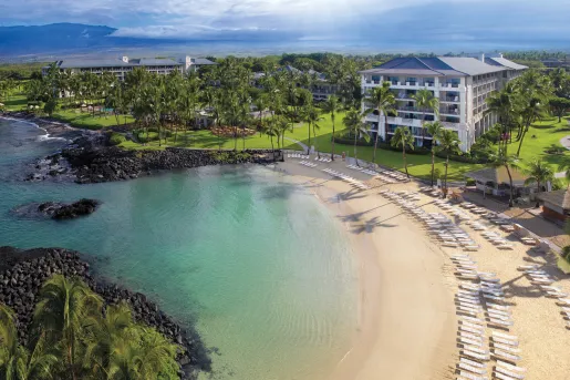 Pool chairs lined up by the coast of the ocean with a large hotel building in the background
