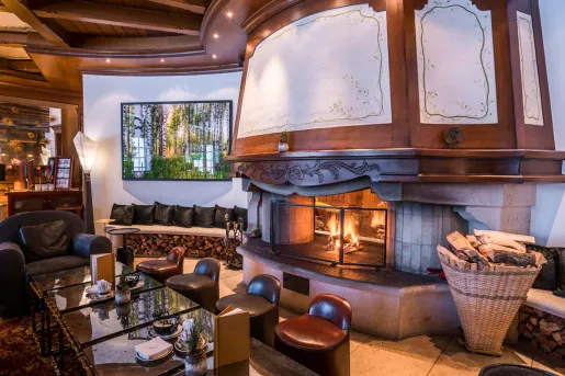 Indoor lounge with cushioned stools around a table with a fireplace behind