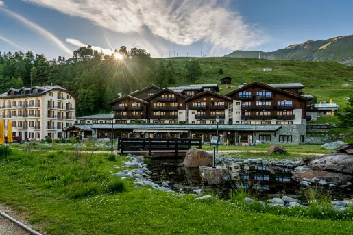 Brown hotel building with a small river and pond, with a wooden bridge in front