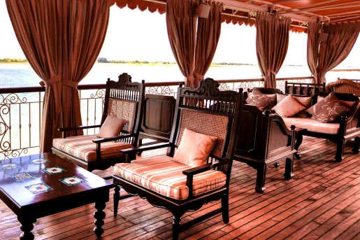 Wooden patio with large, red curtains and cushioned chairs looking out towards a lake