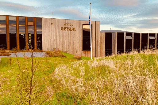 Exterior view of hotel building with a flag pole and grass field in front