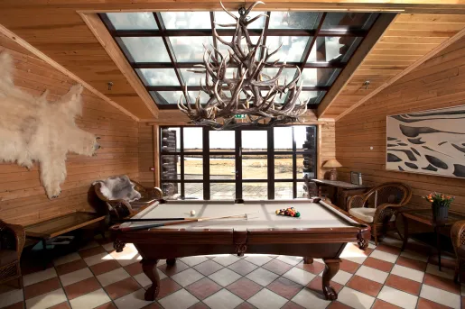 Indoor wooden lodge with a pool table in the center and wooden furniture along the sides