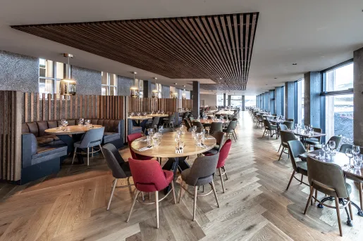 Dining hall with wooden fixtures on the ceiling, and red and black chairs surrounding each table