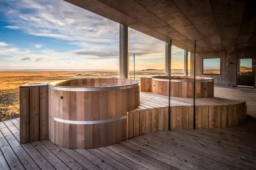 Outdoor wooden sauna with large, stone pillars looking out to an open valley