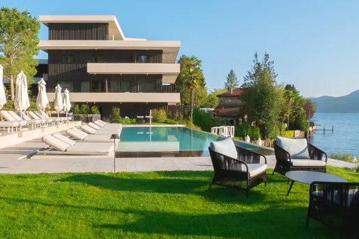 Outdoor pool surrounded by white reclining chairs next to a lake