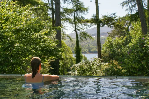 Woman swimming in a pool, looking out to a forest and lake