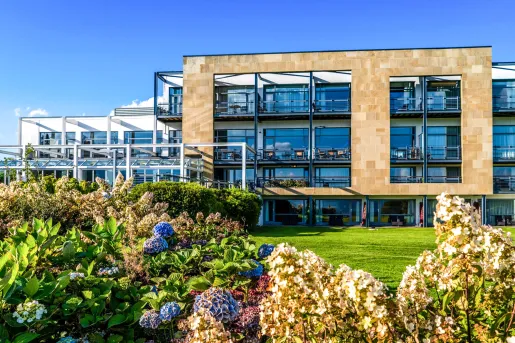 Exterior view of a hotel building with large, glass walls and plants on the ground floor